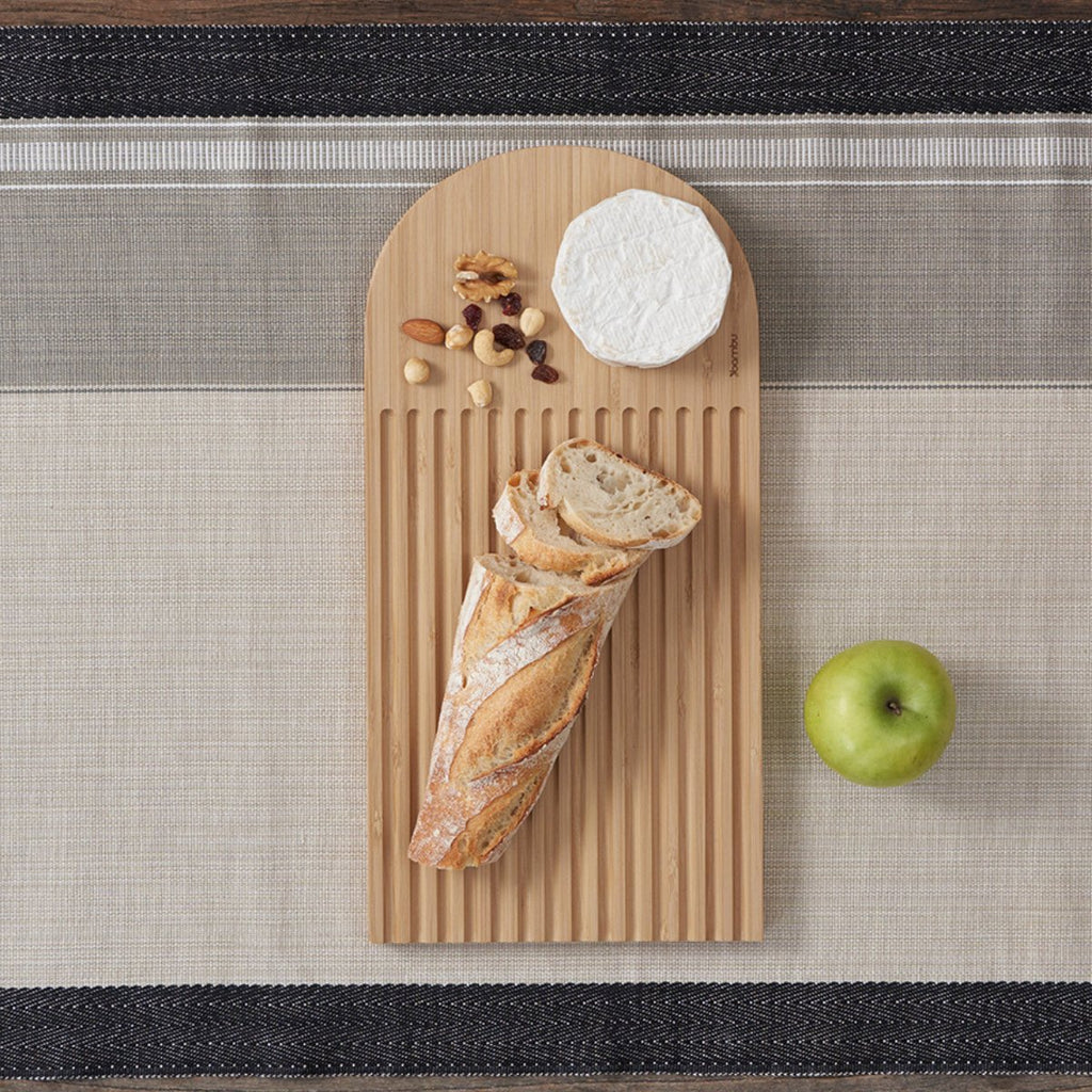 A collection of bamboo cutting boards on a table. The bamboo cutting board has bread and jam jars on it.