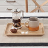 A small bamboo Serving Tray holds a french press and coffee mug next to a pastry .