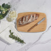 MediumA medium Classic Cutting & Serving Boards has a small loaf of rustic bread on it. A knife is next to the bread, ready to slice and serve. - bambu