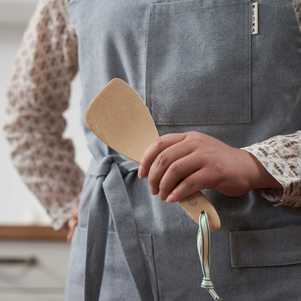 A person in a blue apron holds a bamboo rice paddle