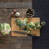 A Medium Undercut Series Cutting Board is used for meal prep. A head of broccoli is chopped on the board, and a head of cauliflower waits nearby - bambu