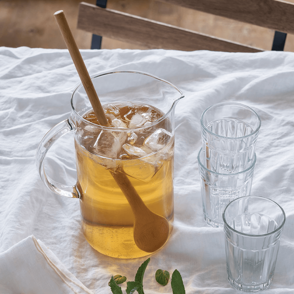 A bamboo Tasting Spoon is used to stir a pitcher of iced tea.