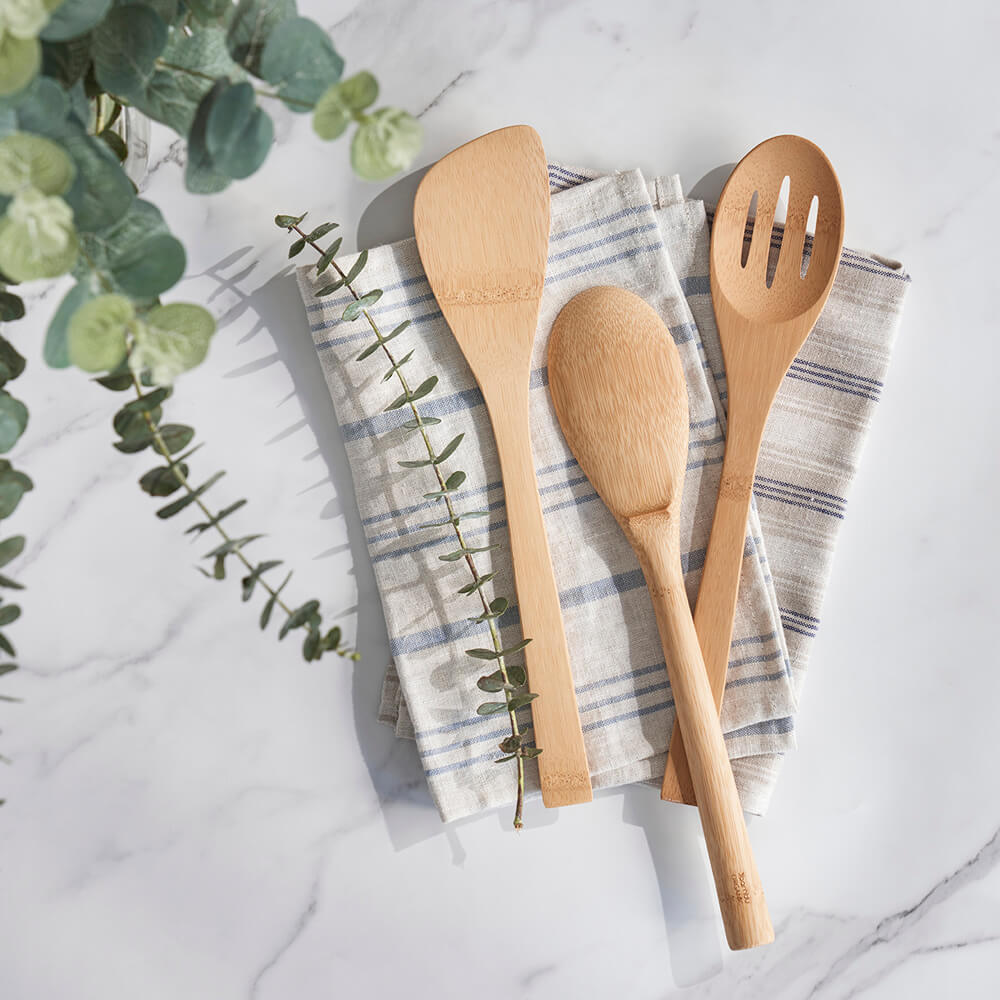 The 'Give It A Rest' Utensil Set is shown resting on a set of striped kitchen towels.- bambu