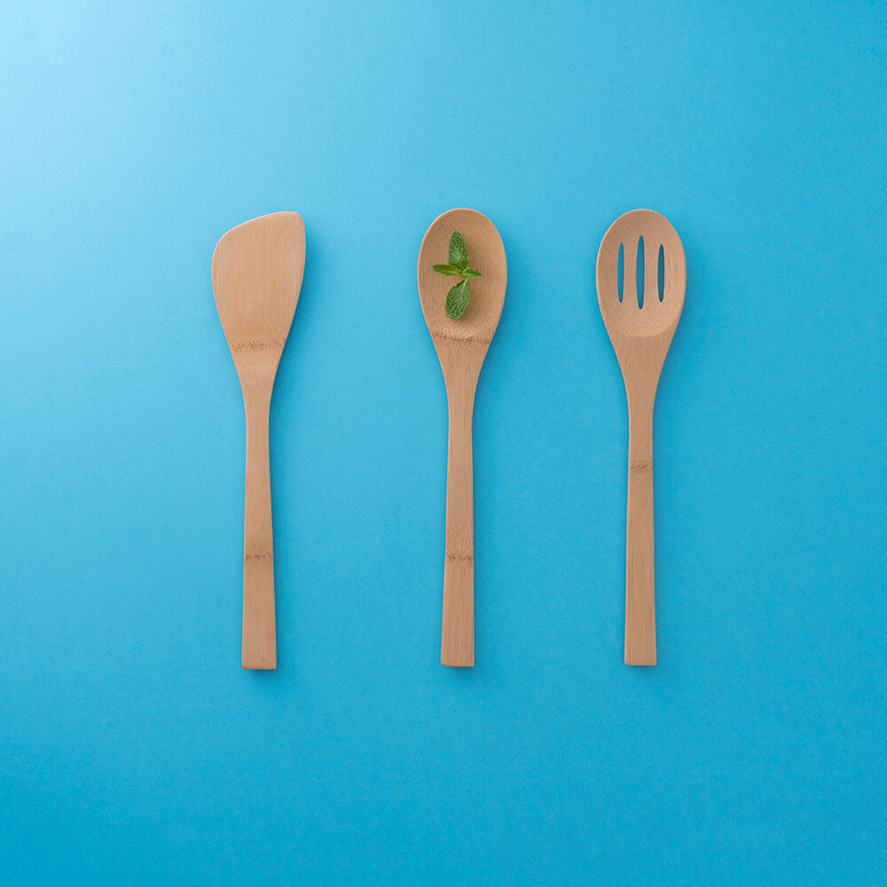 A set of 3 Give it a Rest cooking tools are shown on a vibrant blue background. A sprig of mint is placed on the spoon in the center. bambu