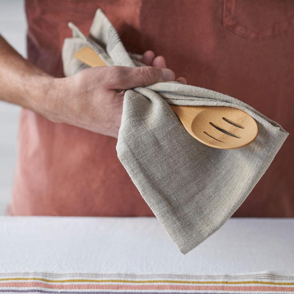 A person is shown holding a 'Give It a Rest' Slotted Spoon in a kitchen towel.