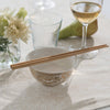 A set of Reusable Bamboo Chopsticks lay across the top of a porcelain bowl. A wine glass, water glass, and small jar of flowers complete the tablesetting.