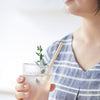 A person in a blue and white top holds a drinking glass filled with lemonade. A Disposable Bamboo Straws is ready for sipping.