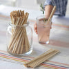 A jar filled with Single Use bamboo straws is set in the middle of a table. A person holds a glass that has a pink beverage, and a single use straw is in the glass.