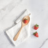 A Bamboo Serving Spoon rests on a white kitchen towel. Several strawberries are arranged on and near the spoon.