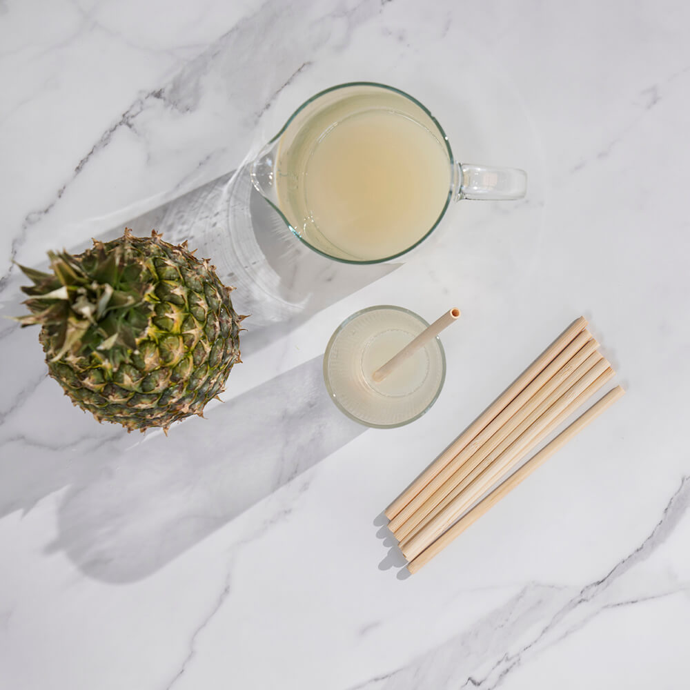 A pitcher of lemonade sits next to a drinking glass. Disposable Bamboo Straws are ready for use with the drink. 