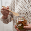 A person uses a reusable bamboo spoon to eat food from a glass jar. bambu