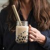A woman holds a glass of Boba Tea with a Reusable Bamboo Jumbo Straw.