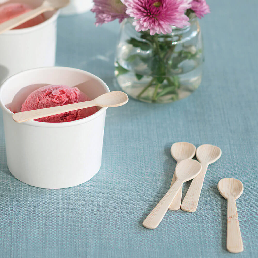 A handful of Veneerware® 4" Tasting Spoons sit near a scoop of ice cream in a paper cup - bambu