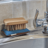 An All-Purpose Cleaning Brush rests on a Teal LongLife Sponge at the side of a stainless steel sink.