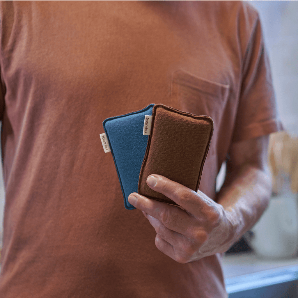 A person in a rust colored shirt holds a pair of LongLife sponges, showing the teal and nutmeg colors that are new for fall 22.