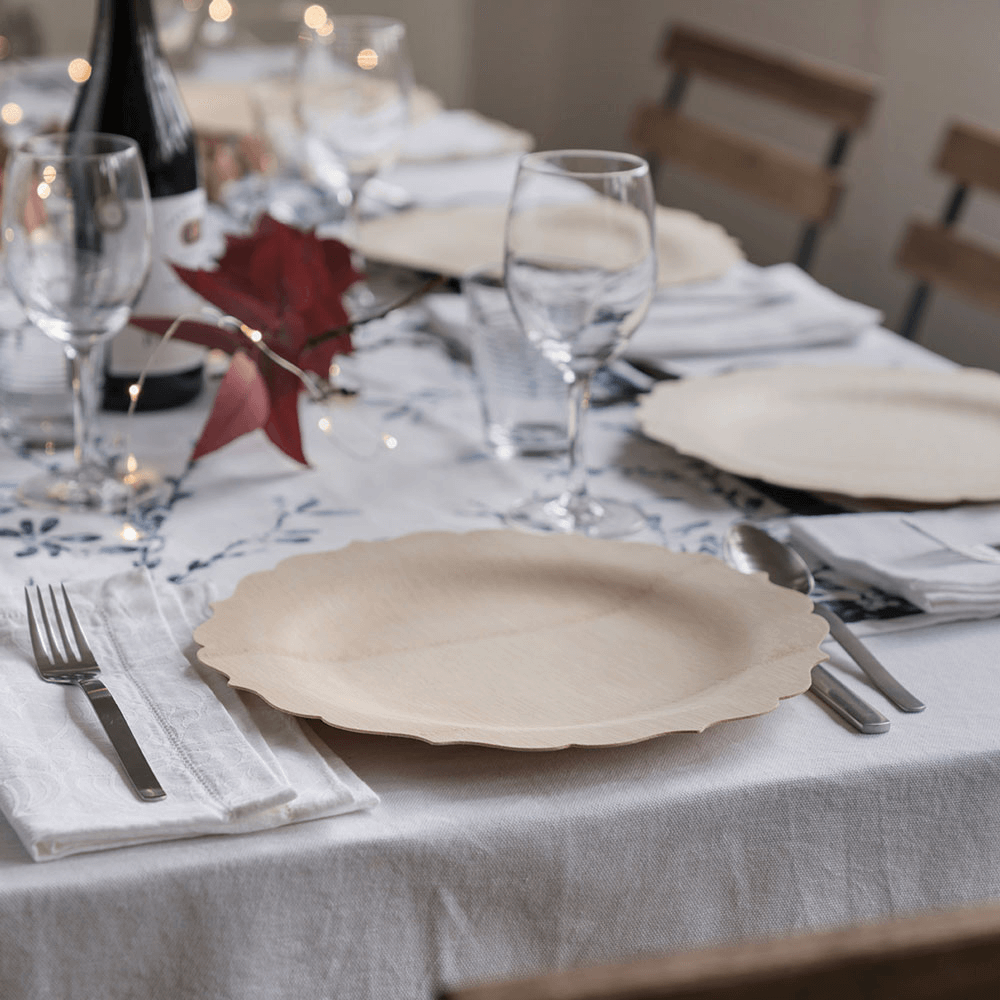 A white covered table is set with 11" Veneerware® Fancy Bamboo Plates. Each place setting is completed witha  white cloth napkin and a set of silver flatware. 