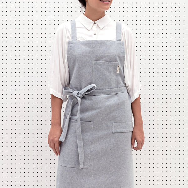 A woman models a MEEMA Crossback Apron made with Upcycled Denim.