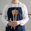 A person in a white shirt and denim apron holds an All Purpose Bamboo Mixing Spoon and a spoontula