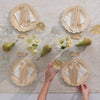 A table is set for 4. Each setting has a 9" Veneerware® Fancy Bamboo Plate, a cocktail napkin, and a set of Veneerware Cutlery. There are glass water cups, two small vases of flowers, and 3 pears on the table.
