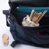 An eat/drink tool kit is peeking out from a cross-body tote bag. The spork lays on the table next to the bag. 