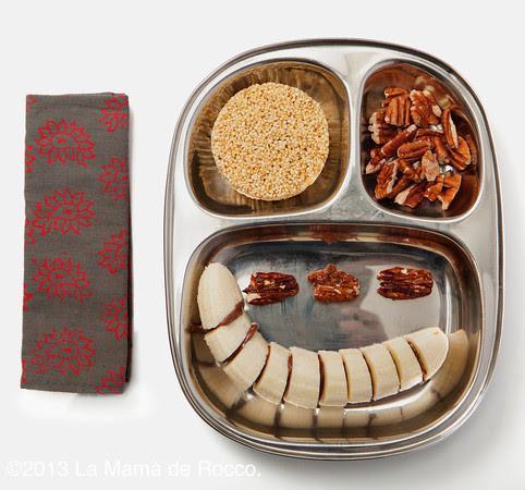 A cut banana with peanut butter, nuts. and a rice cake are served on an ECOlunchbox Kids Lunch Tray.