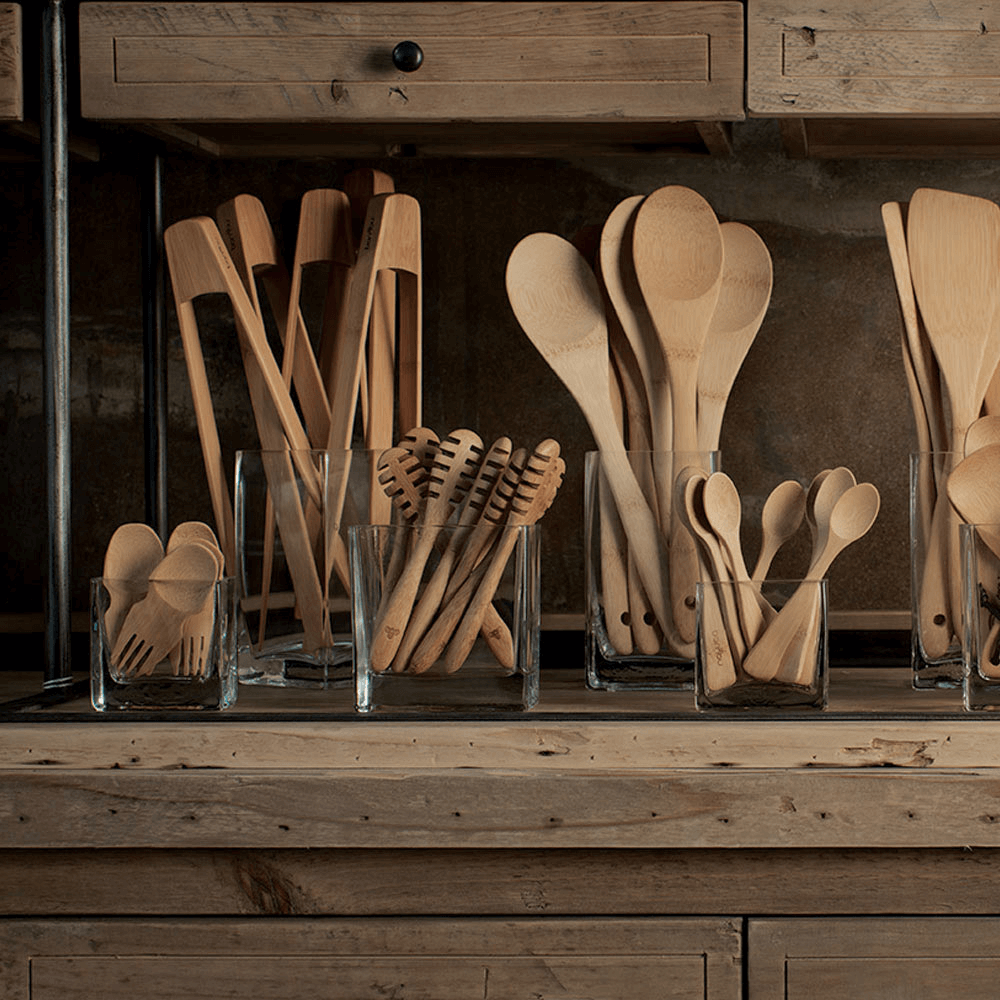 A wooden countertop holds jars filled with bamboo utensils. Large Tongs are featured in this display.